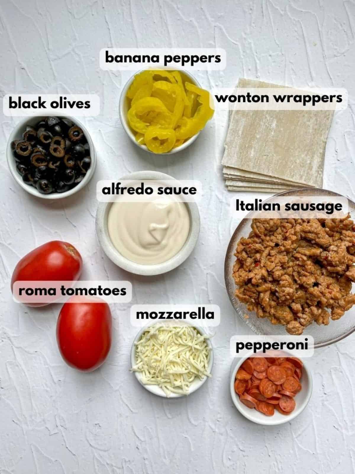 Ingredients needed to make Italian nachos: ground sausage, alfredo sauce, wonton wrappers, black olives, tomatoes, cheese, and pepperoni.