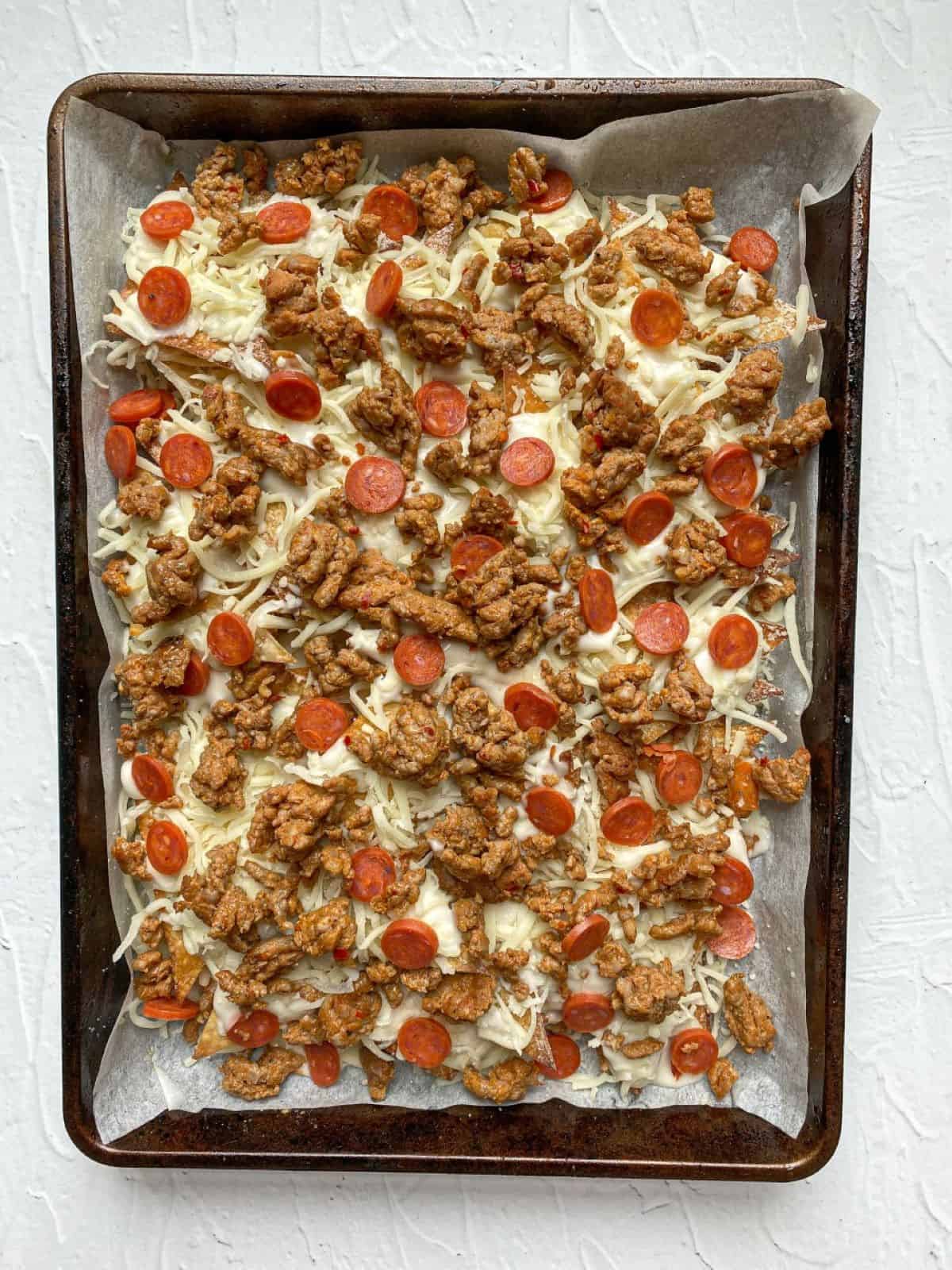 Wonton nachos on a baking sheet with alfredo sauce, mozzarella, Italian sausage, and mini pepperoni.