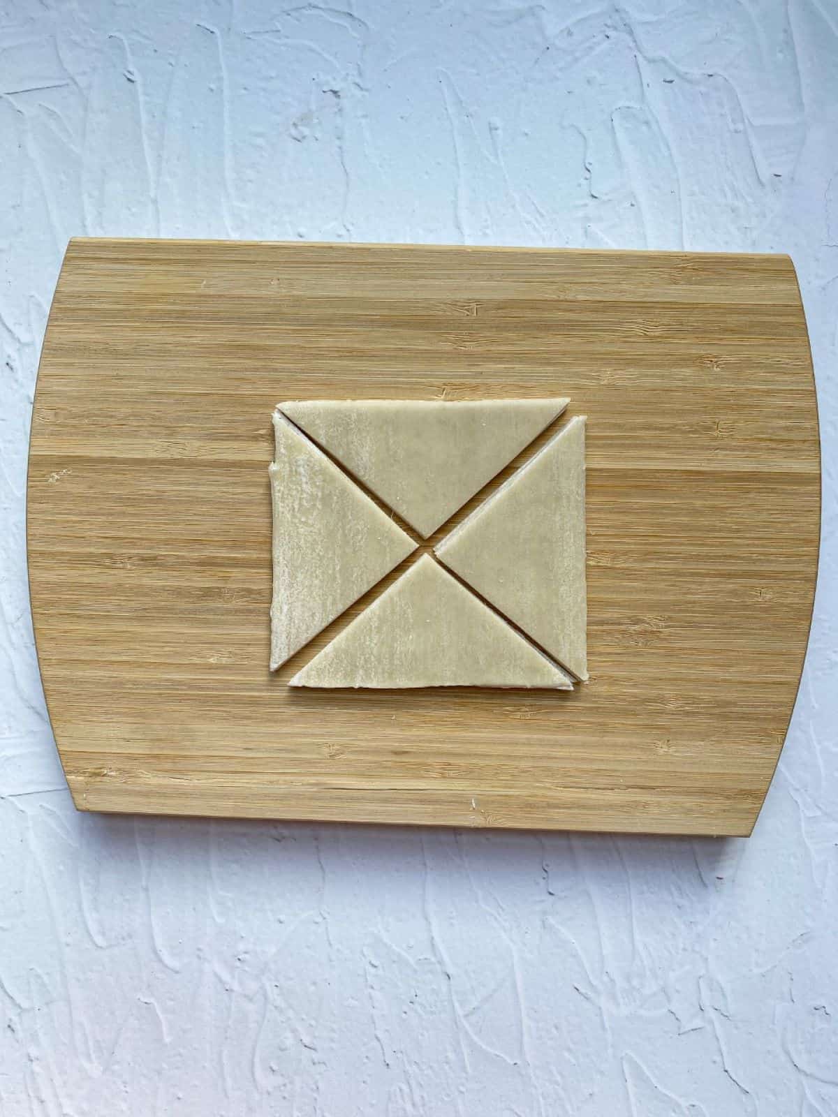 A wonton wrapper on a cutting board cut into four triangle shaped chips.