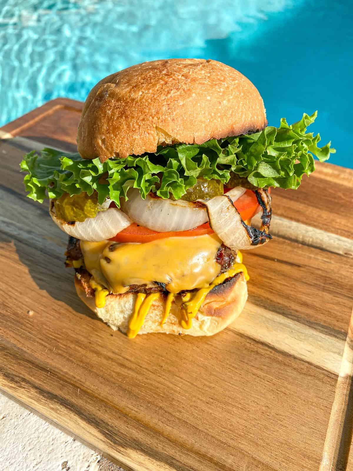 Cheeseburger on a cutting board with beef patty, pickles, grilled onions, fresh tomato, and lettuce.