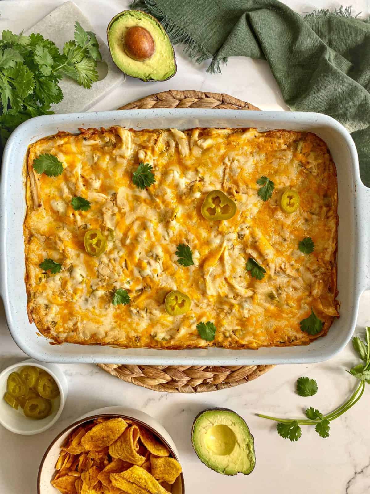 Cooked sour cream chicken enchilada casserole in a baking dish with chips and avocado on the side.