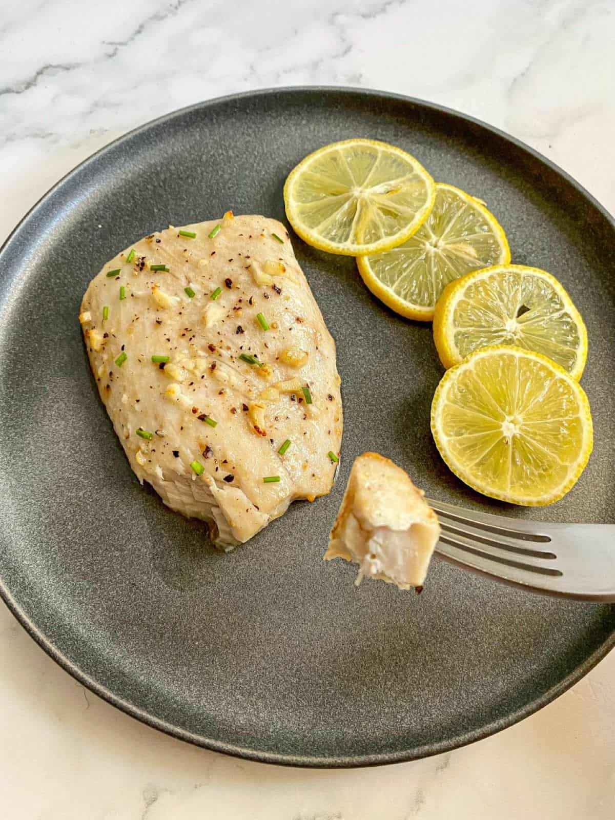 A fish fillet on a plate with lemons on the side. A fork has a piece of fish on it.