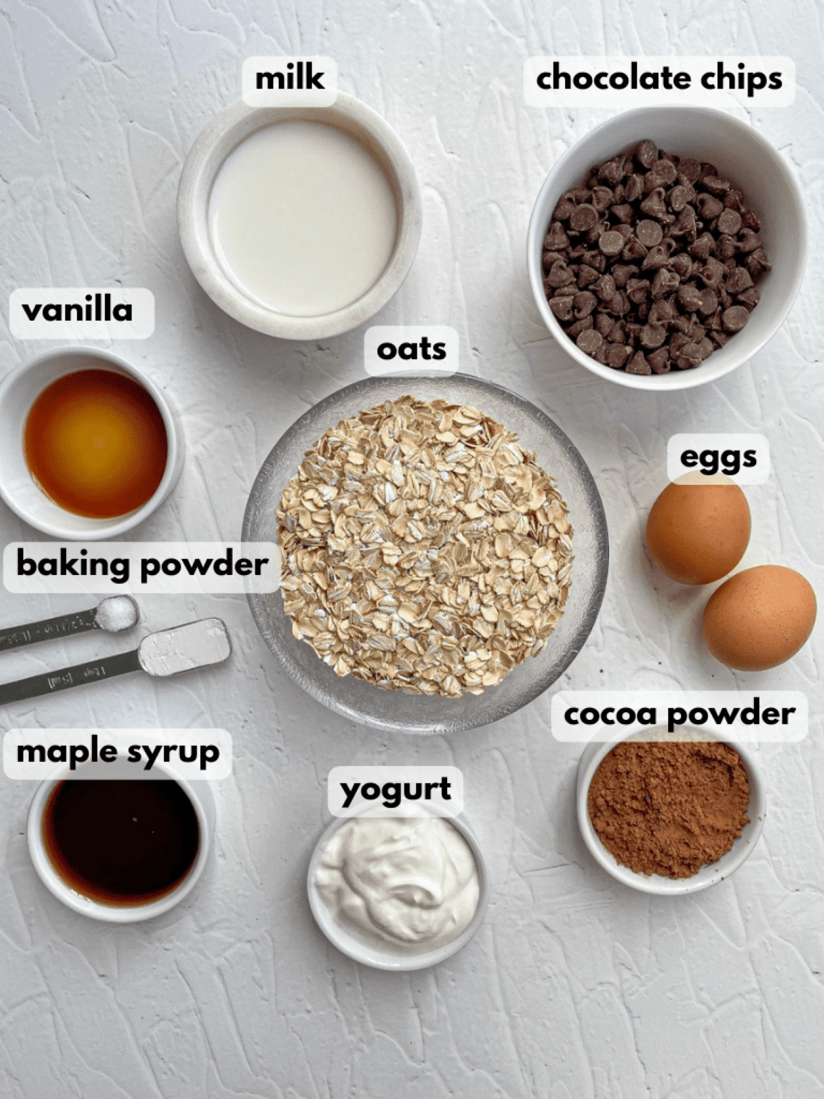 Chocolate Baked Oatmeal Ingredients: oats, milk, eggs, chocolate chips, cocoa powder, yogurt, vanilla extract, maple syrup, and baking powder.