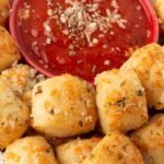 Pizza dough bread bites on a plate with a bowl of red marinara.
