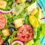 Green salad in a bowl with tomatoes, red onions, croutons, and banana peppers.