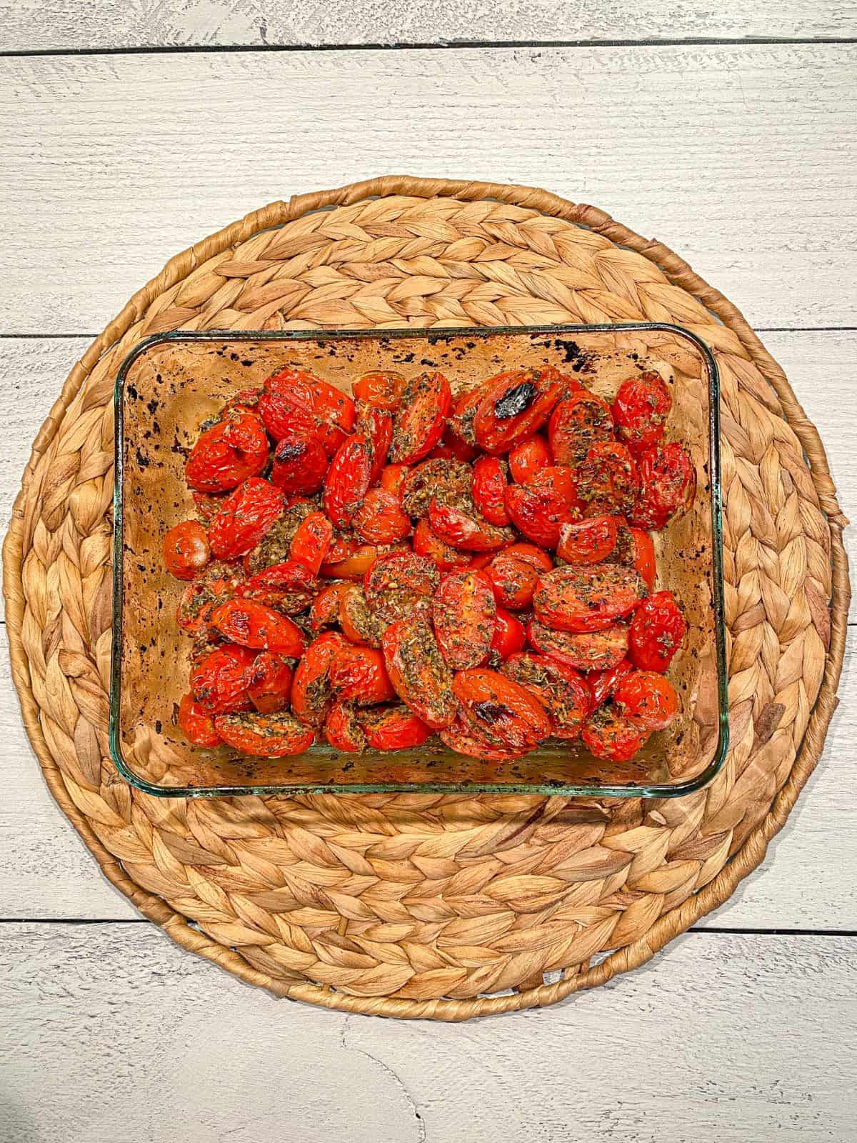 Roasted cherry tomatoes in a baking dish. Tomatoes are blistered and seasoned with Italian seasoning.