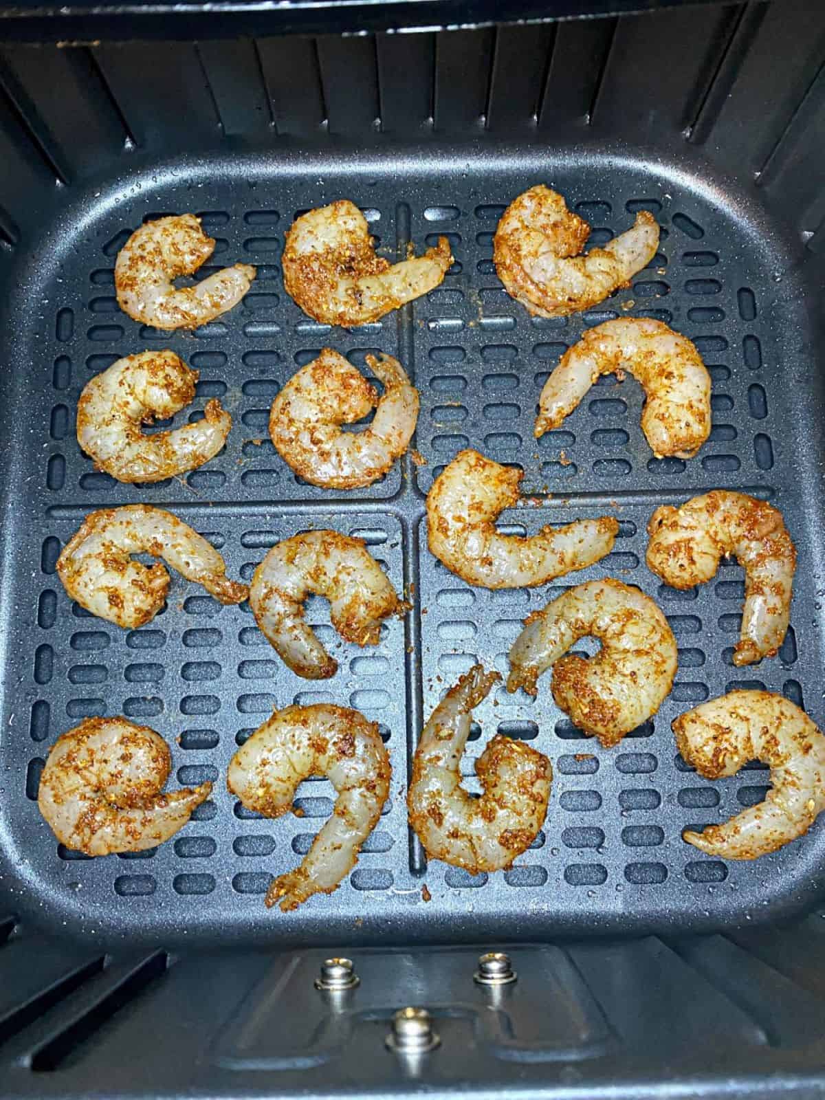 Raw seasoned shrimp in air fryer basket.