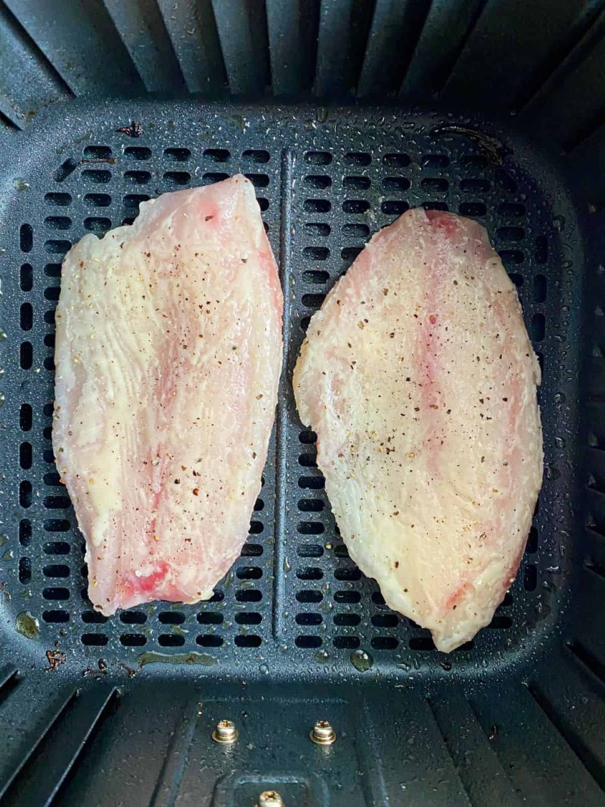 Frozen fish in an air fryer basket seasoned with salt, pepper, and butter.