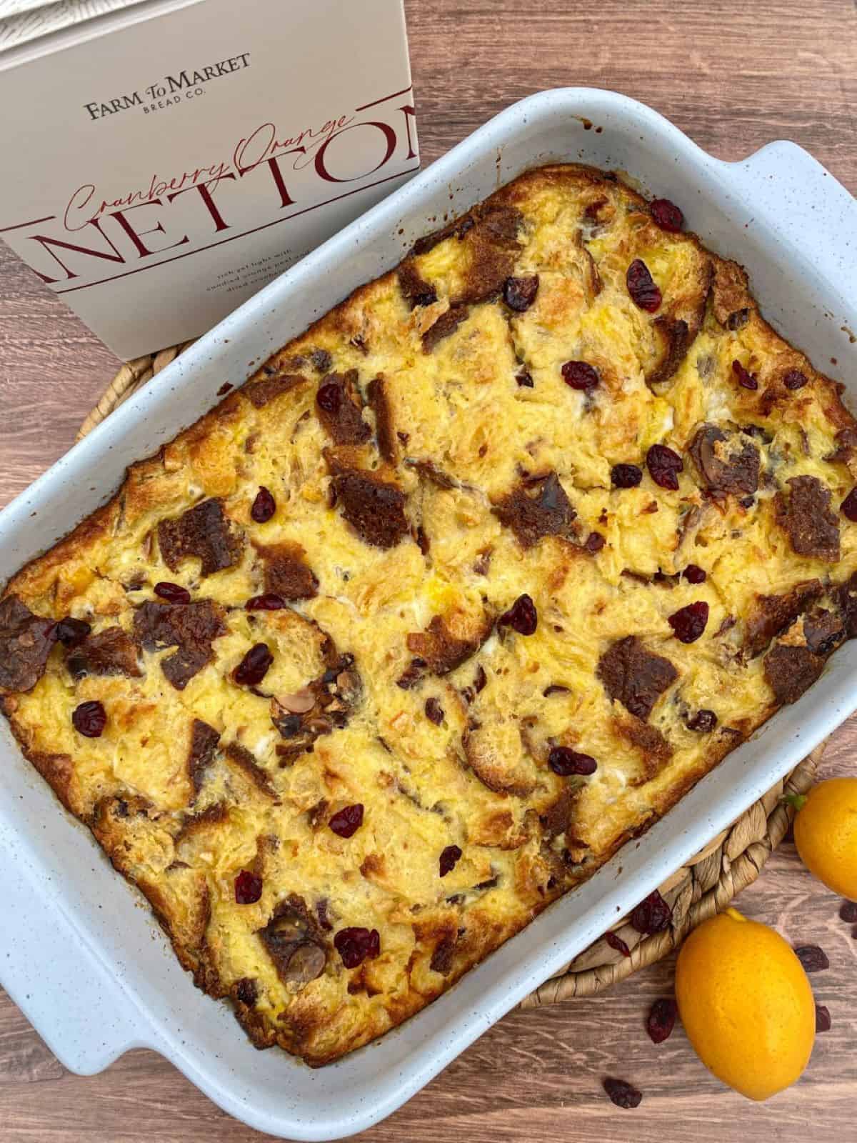 Cranberry orange panettone bread pudding with a bread box and lemons around the baking dish.