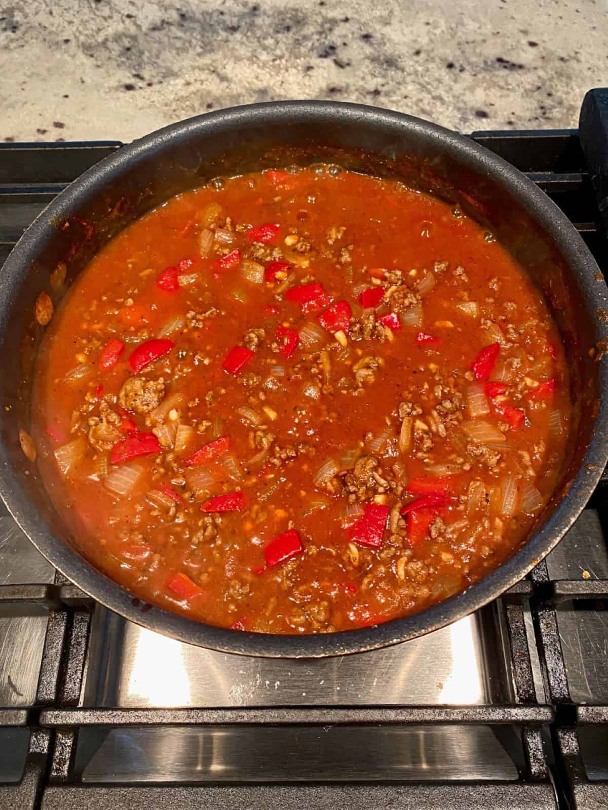 Homemade sloppy joes sauce brought to a boil and simmering in a skillet on the stove.