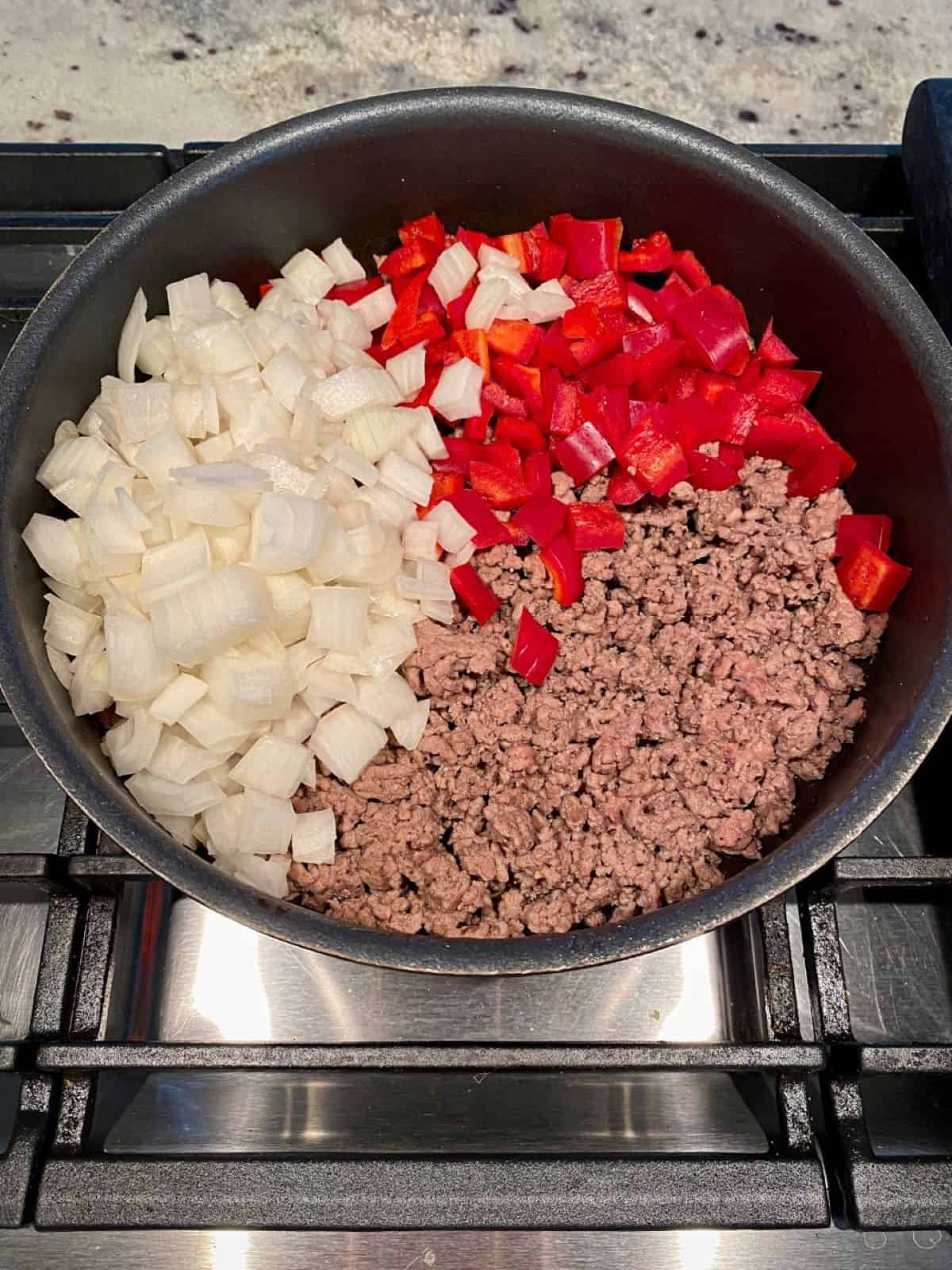 Ground beef browning in a skillet with onions and red bell peppers.