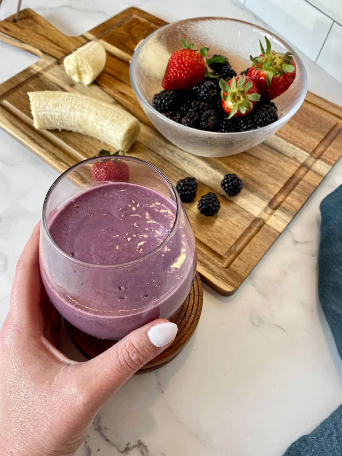 A hand grabbing a purple smoothie made with berries.