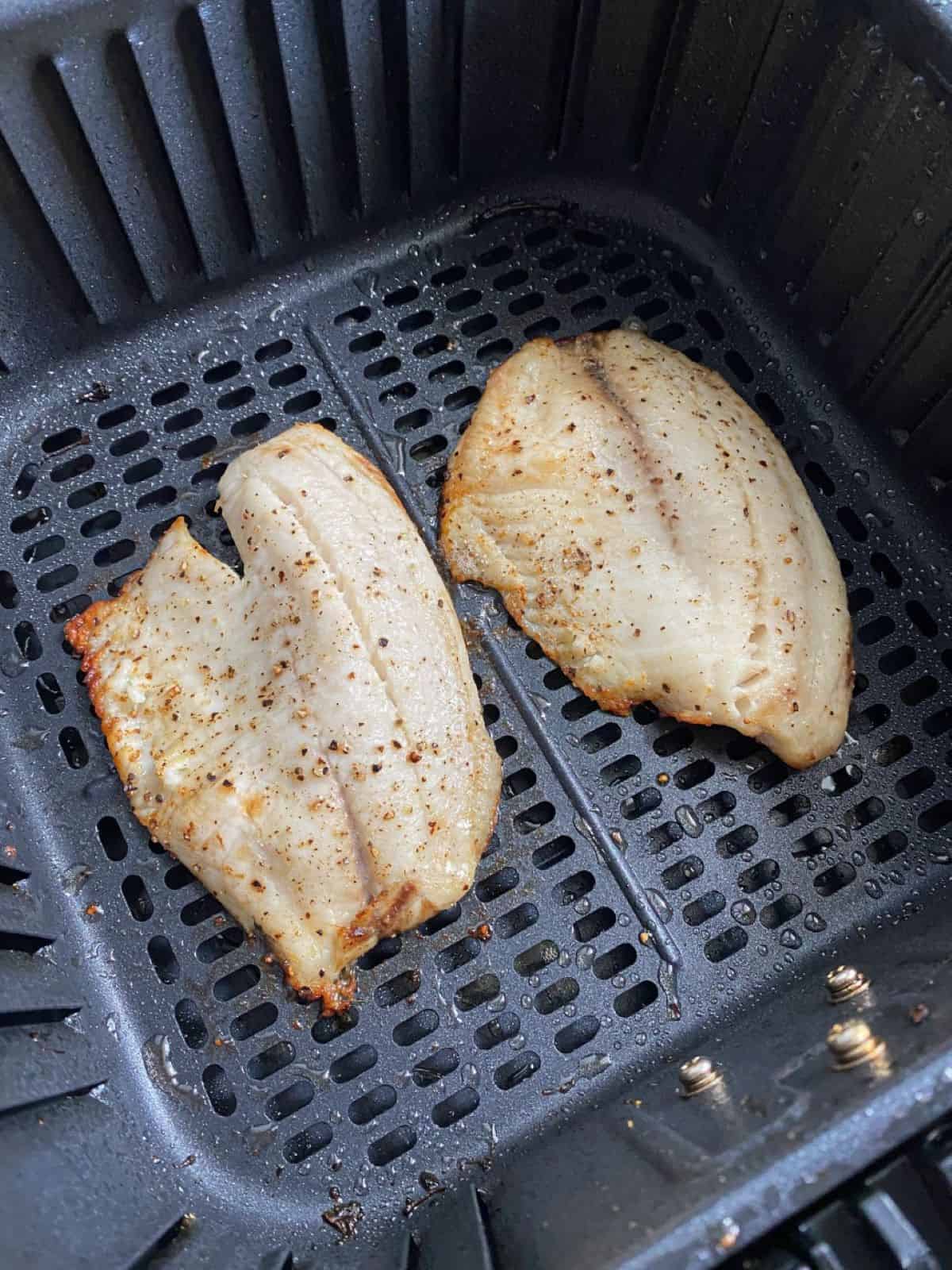 Two cooked fish fillets in an air fryer basket.