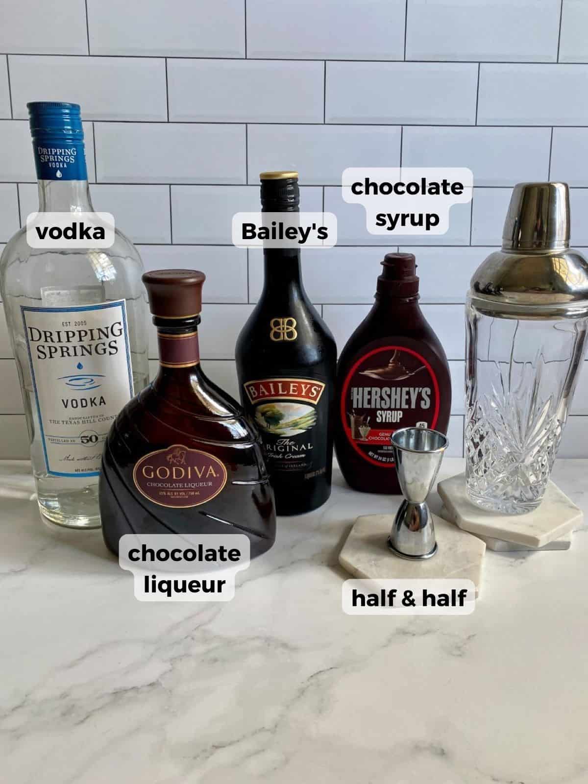 All liquor and liqueur bottles needed to make this martini with a cocktail shaker and jigger on the side.