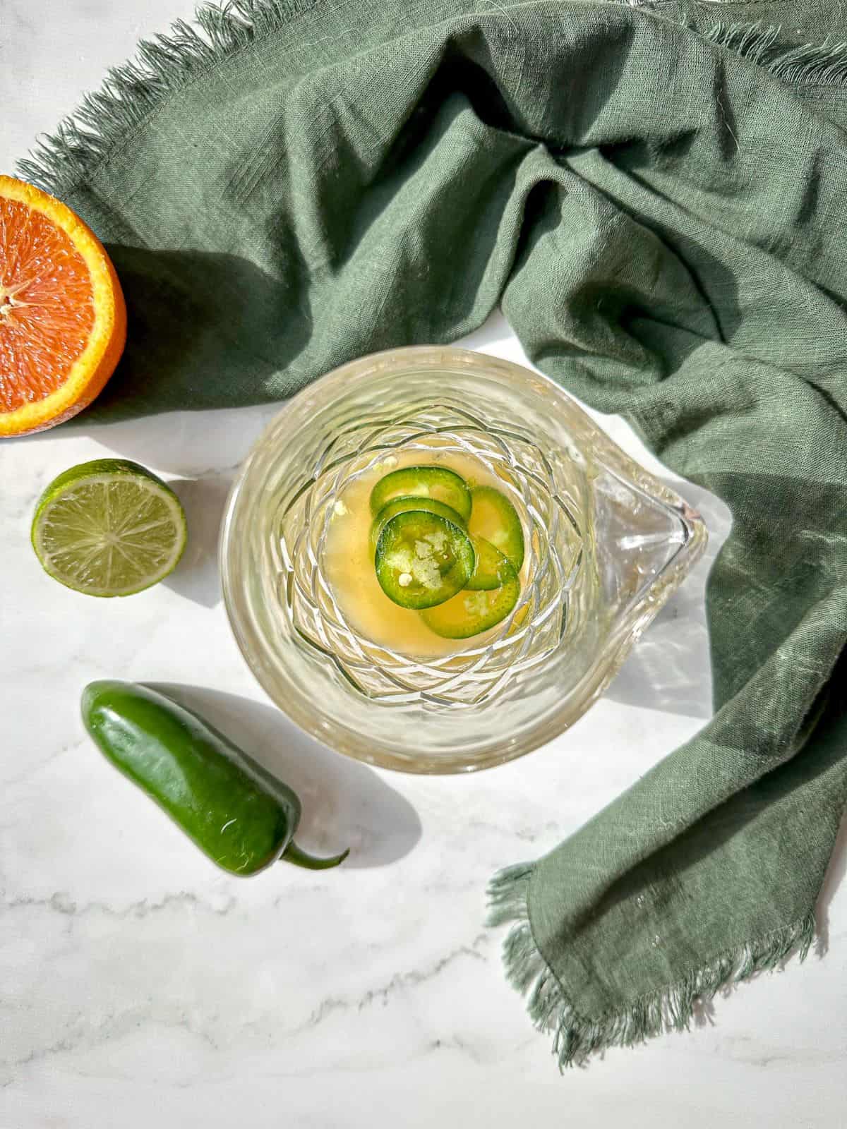 Tequila, lime juice, orange juice, and jalapeno slices in a cocktail shaker.