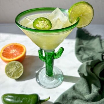 Skinny spicy margarita recipe in a green cactus shaped glass. It's garnished with a jalapeno slice and a lime wedge.