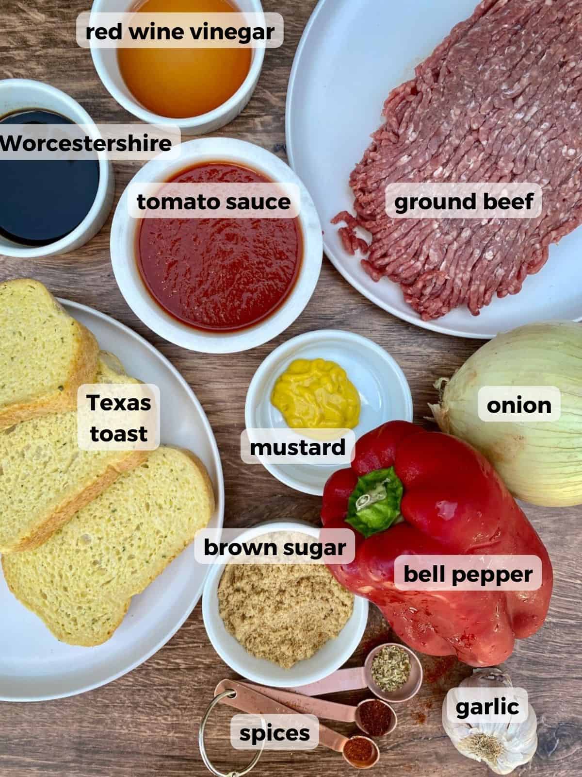 Ingredients needed to cook sloppy joes on Texas toast. Ground meat, onions, peppers, brown sugar, bread, sauce and vinegar are on a wooden table.