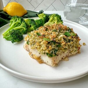 Panko crusted cod on a plate with a side of broccoli. A green towel, glass of water, and lemon are in the background.