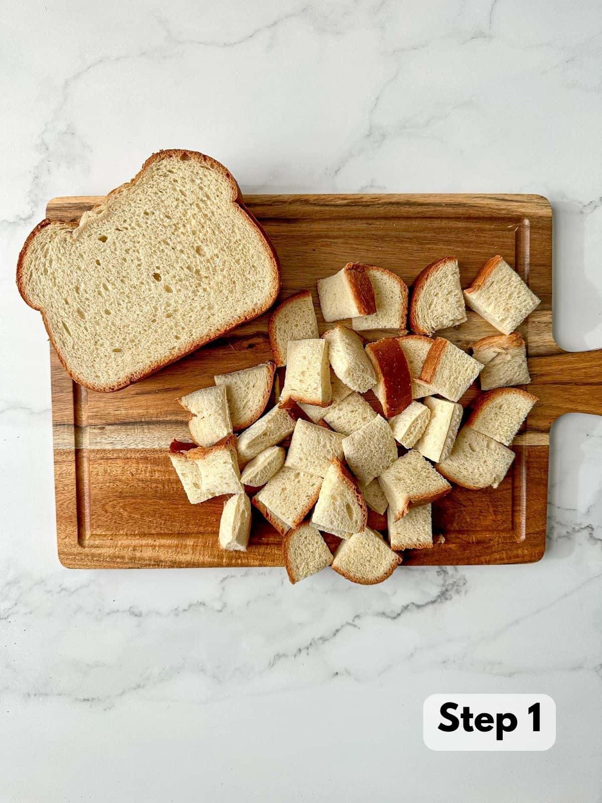 Slices of brioche bread and bread cubes chopped into 1-inch wide pieces on a wooden cutting board.