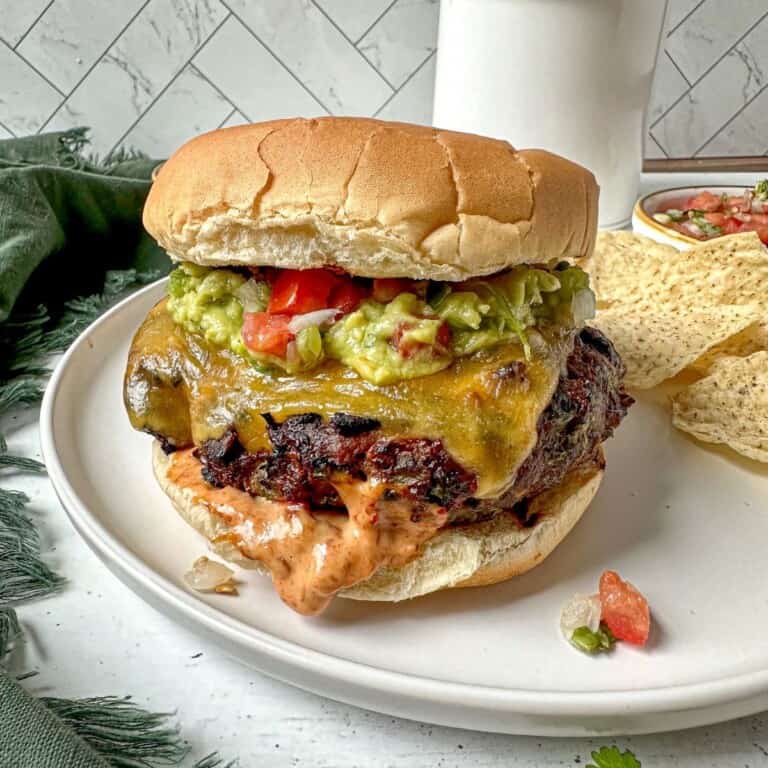 Southwest burger with chipotle mayo, guacamole, and pico de gallo on a white plate with tortilla chips.