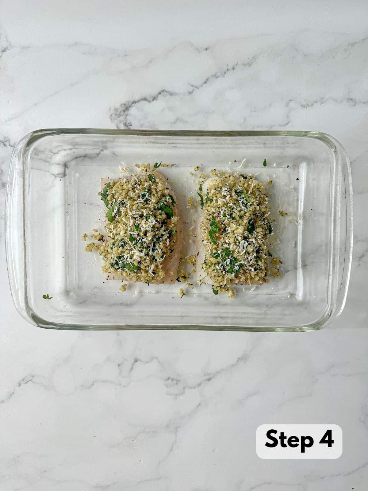 Two uncooked cod topped with panko and parmesan crust in a baking dish.
