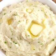 A white bowl filled with creamy mashed potatoes with a pad of melted butter on top.