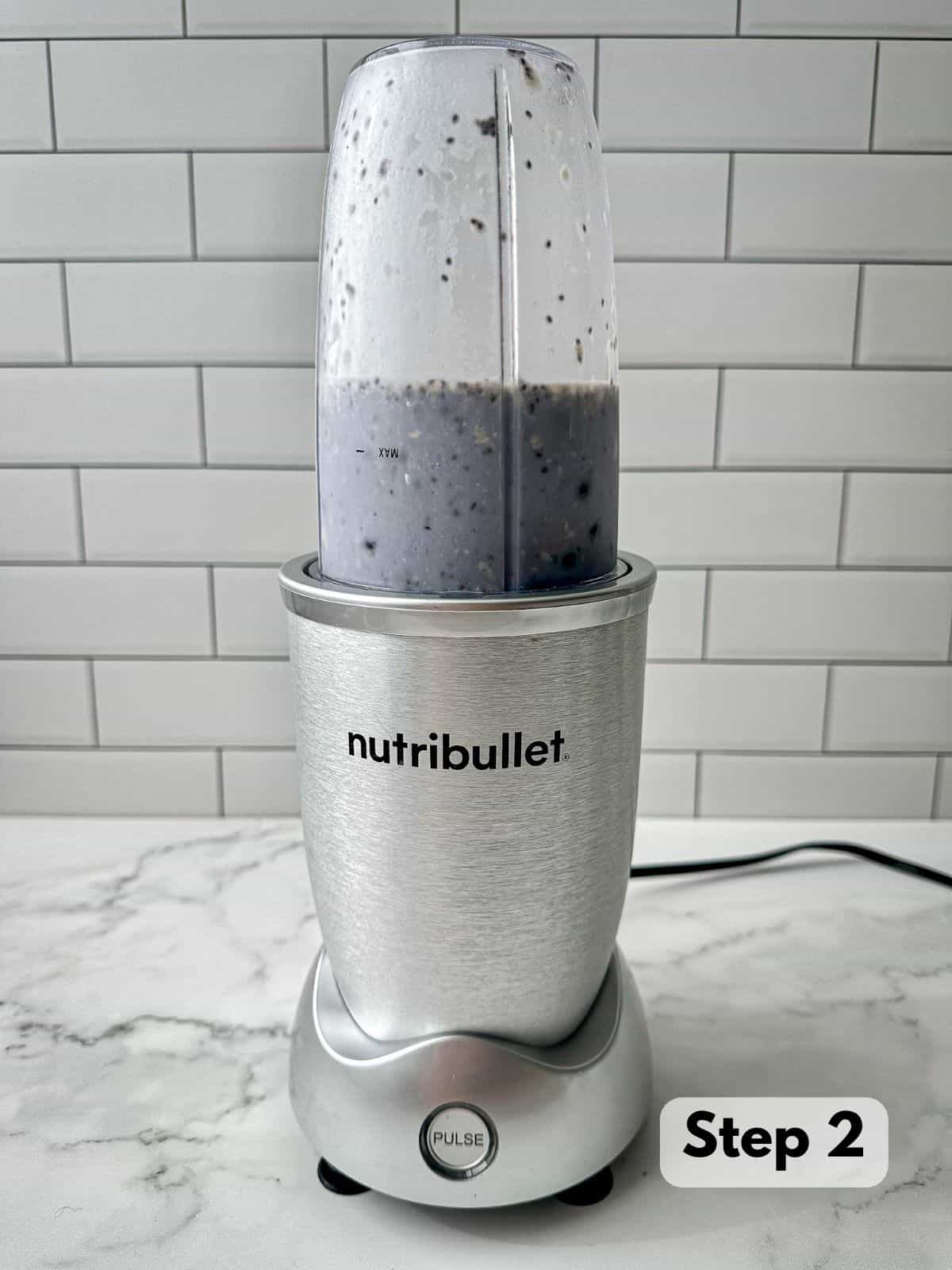 A blue liquid with blueberries, almond milk, chia seeds, and Brazil nuts in a Nutribullet blender.