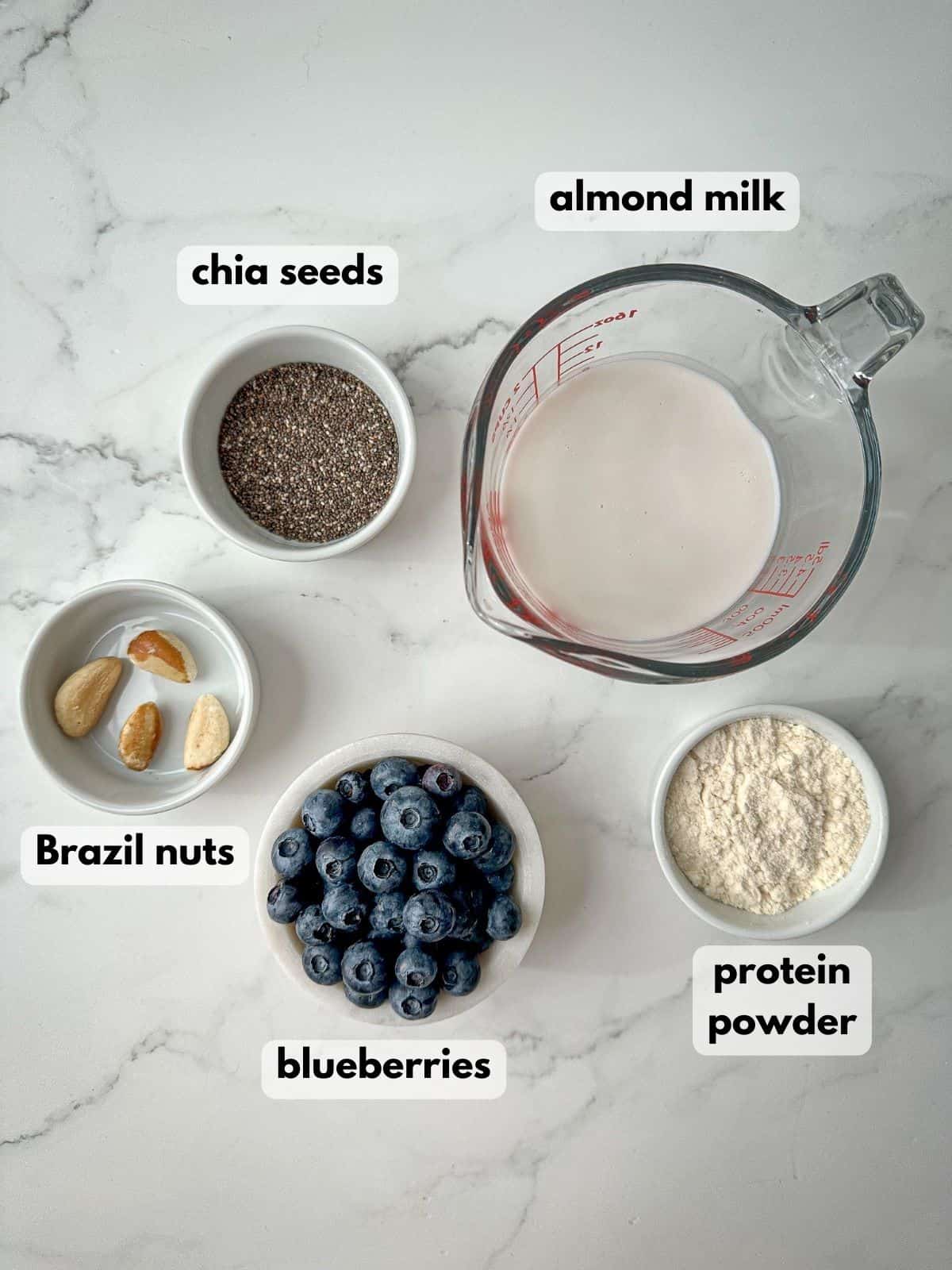 Ingredients needed to make a blueberry protein shake include blueberries, almond milk, chia seeds, and Brazil nuts.