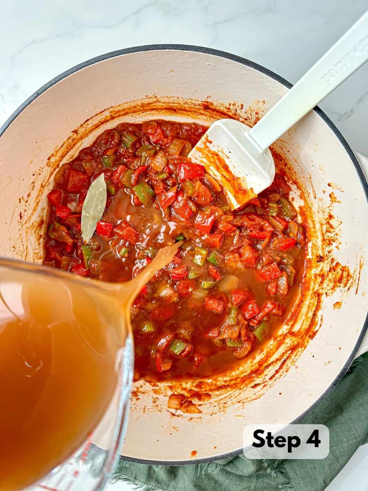 Chicken stock being poured into a large pot with vegetables and Cajun seasonings.