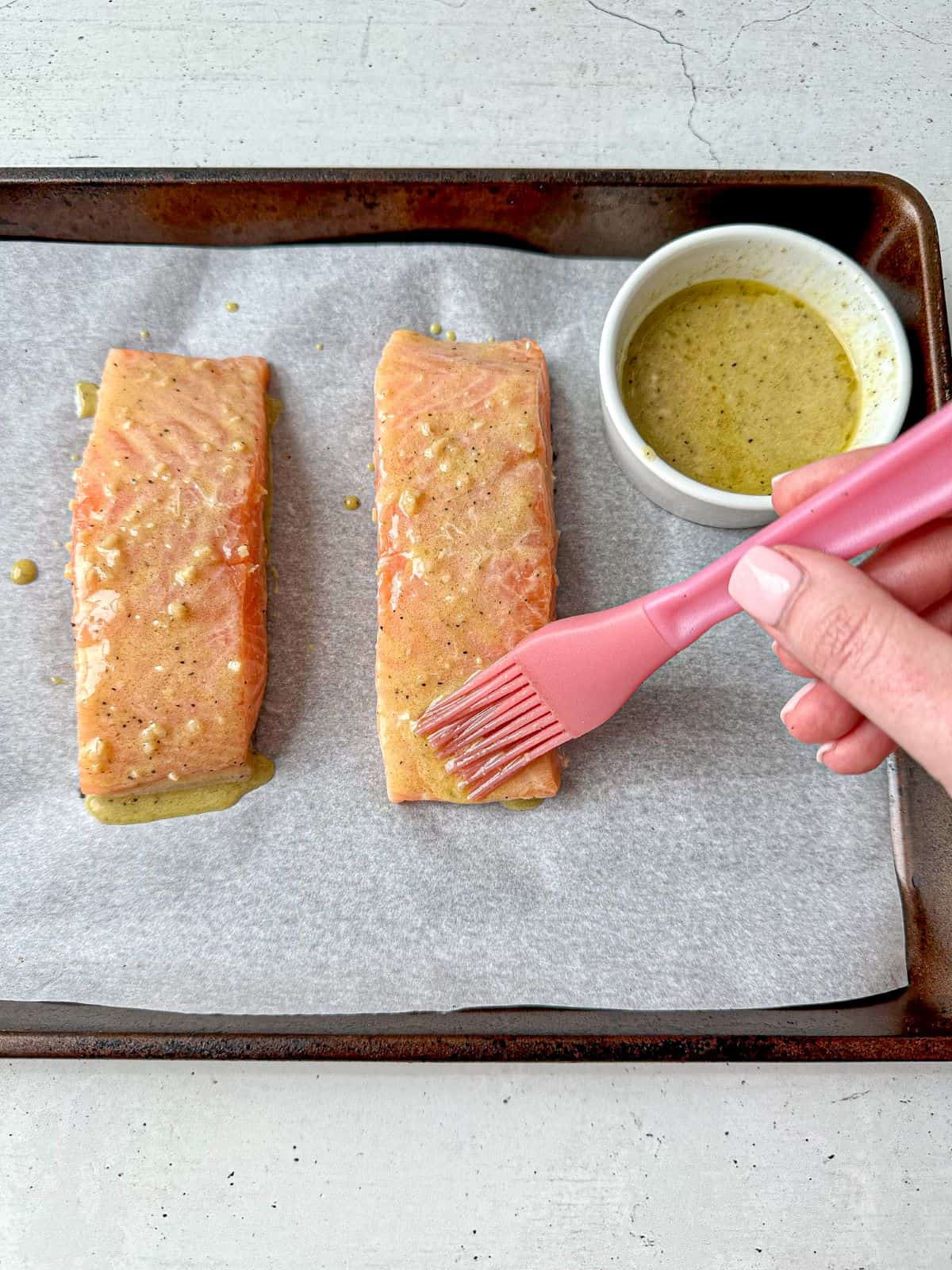 A hand is using a pastry brush to brush on the salmon marinade.