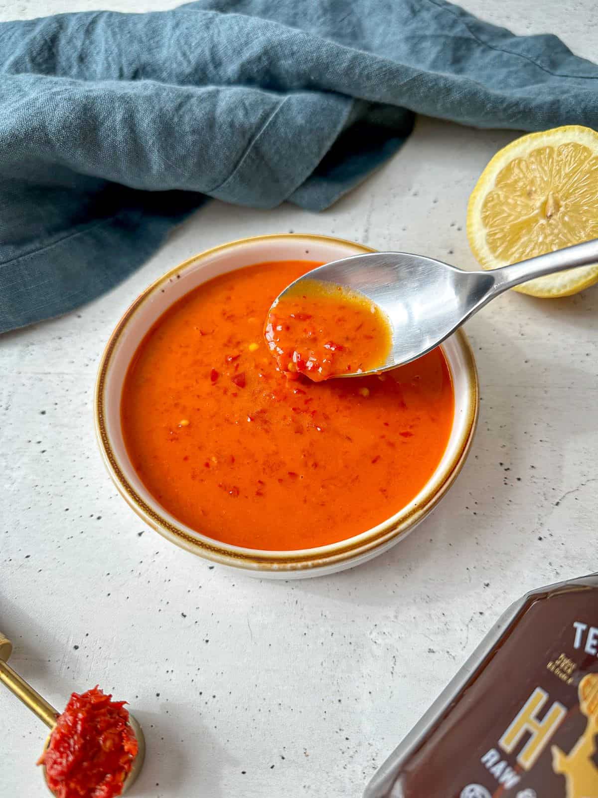 Bright orange-red sauce in a bowl with a silver spoon dipping into the dressing.