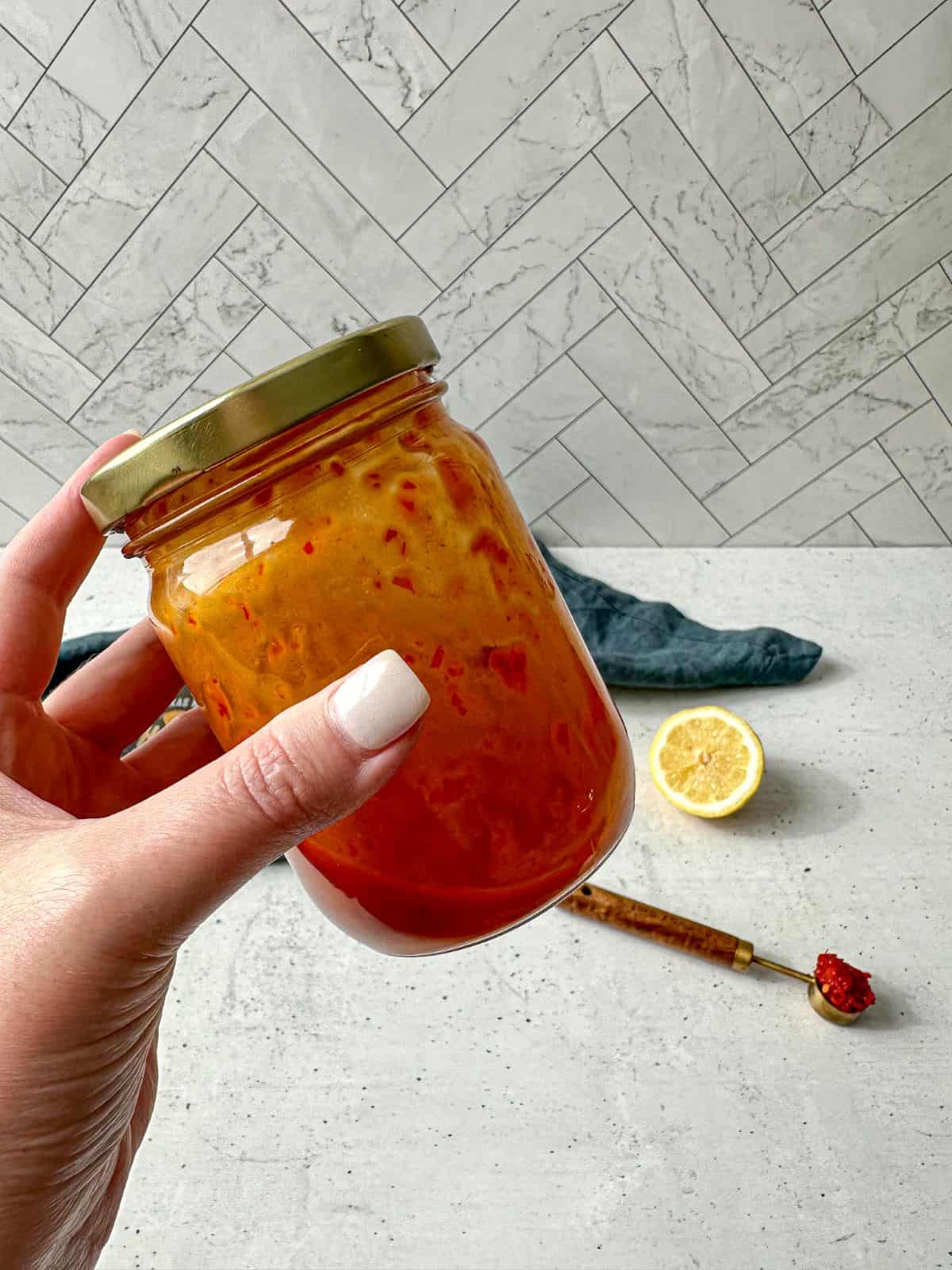 Harissa vinaigrette in a clear glass jar with a lid. The dressing has been shaken and a hand is holding the jar.