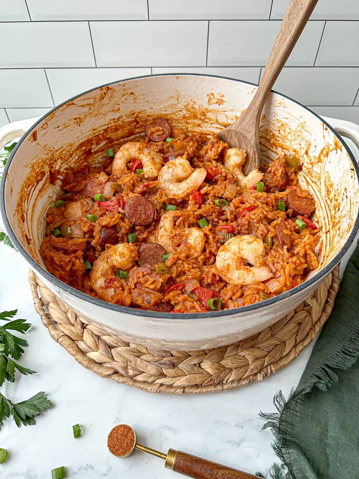 Sausage and shrimp jambalaya in a large white pot with a wooden spoon.