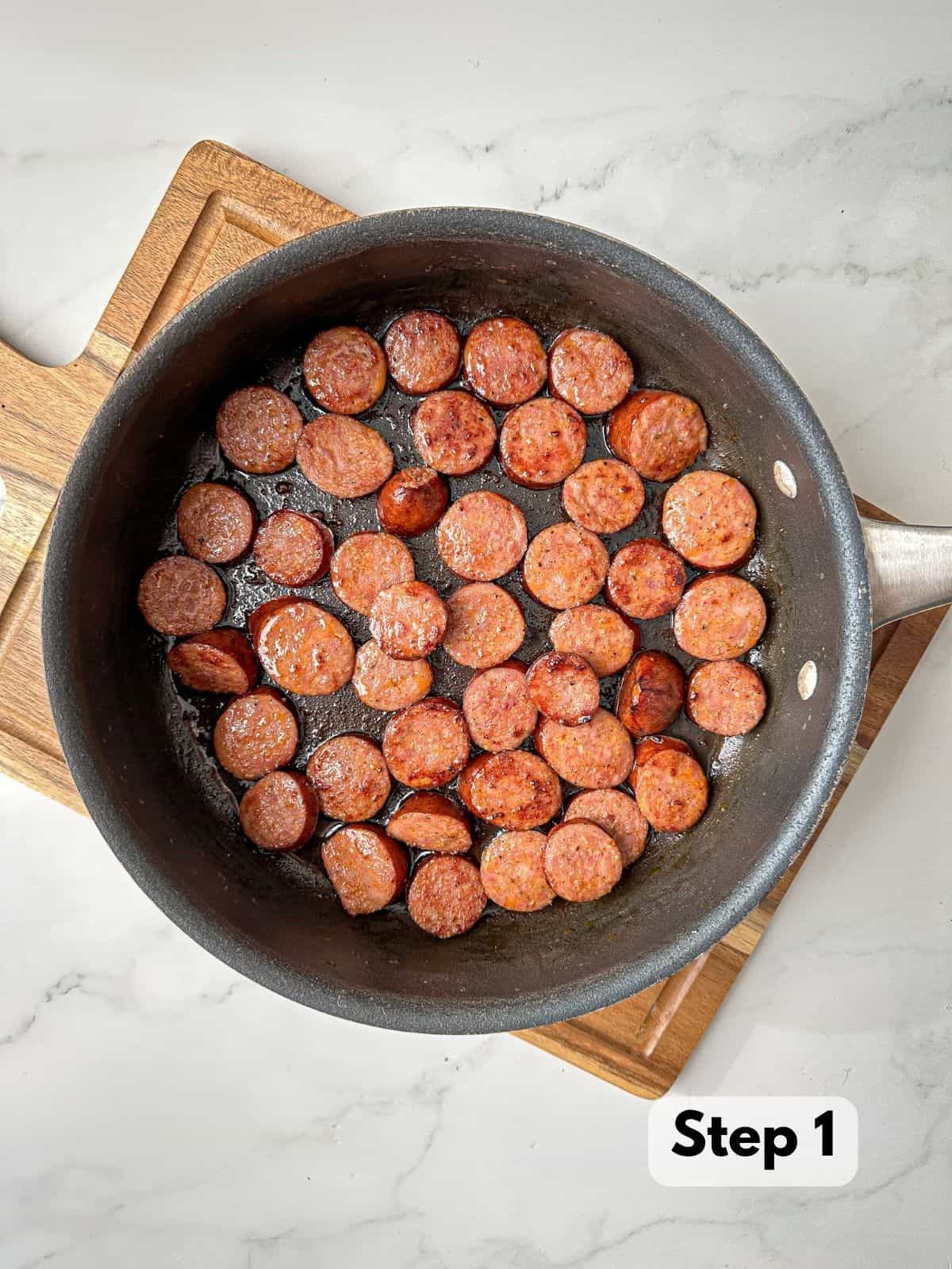 Slices of andouille sausage cooking in a large skillet.