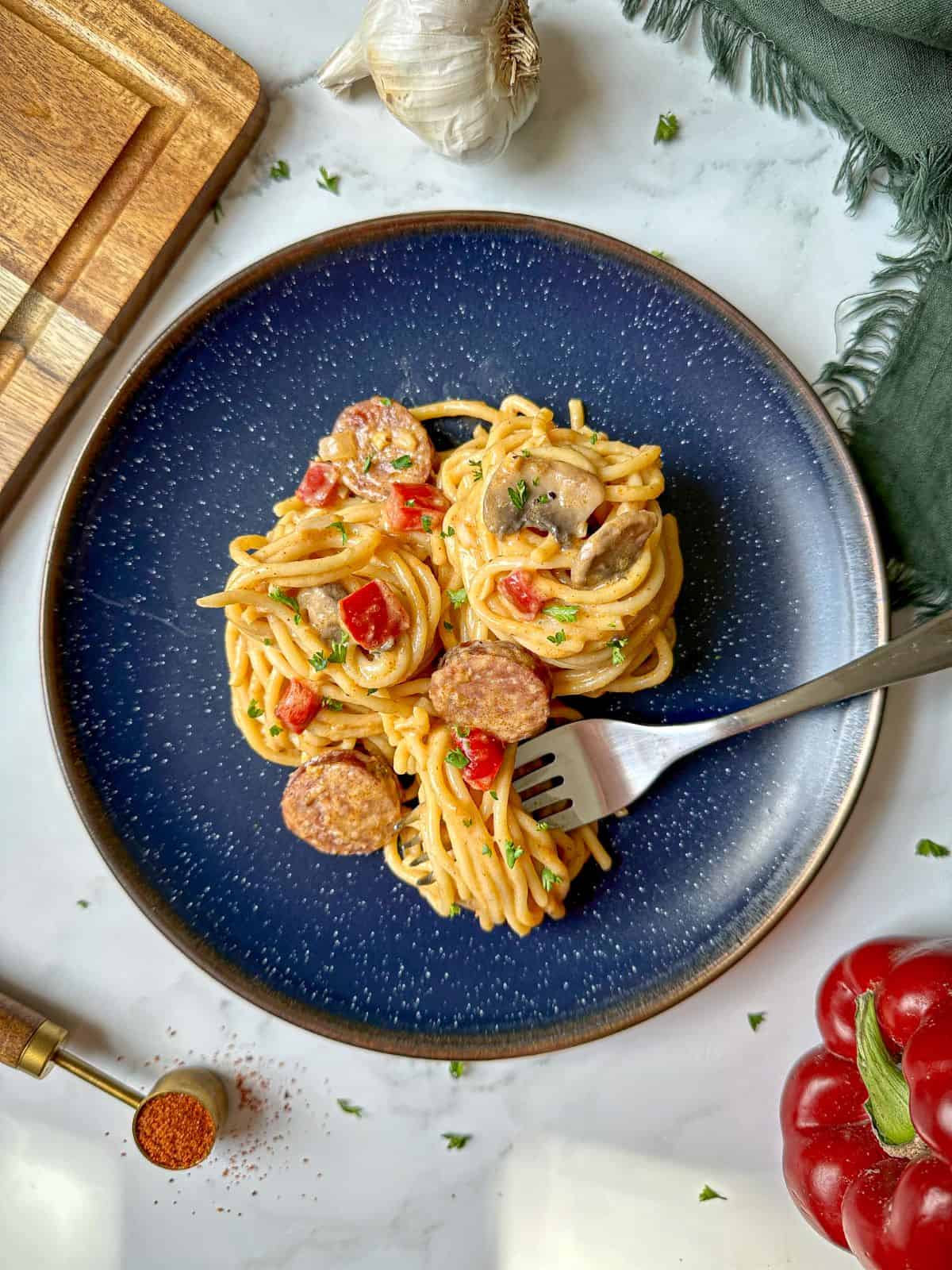 Spaghetti with sausage and red peppers on a round plate. The creamy spaghetti is wrapped around a fork on the plate.