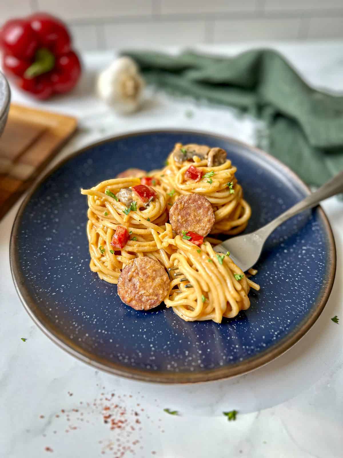 A blue plate with spaghetti, sausage, and peppers. The creamy spaghetti is wrapped around a fork on the plate.