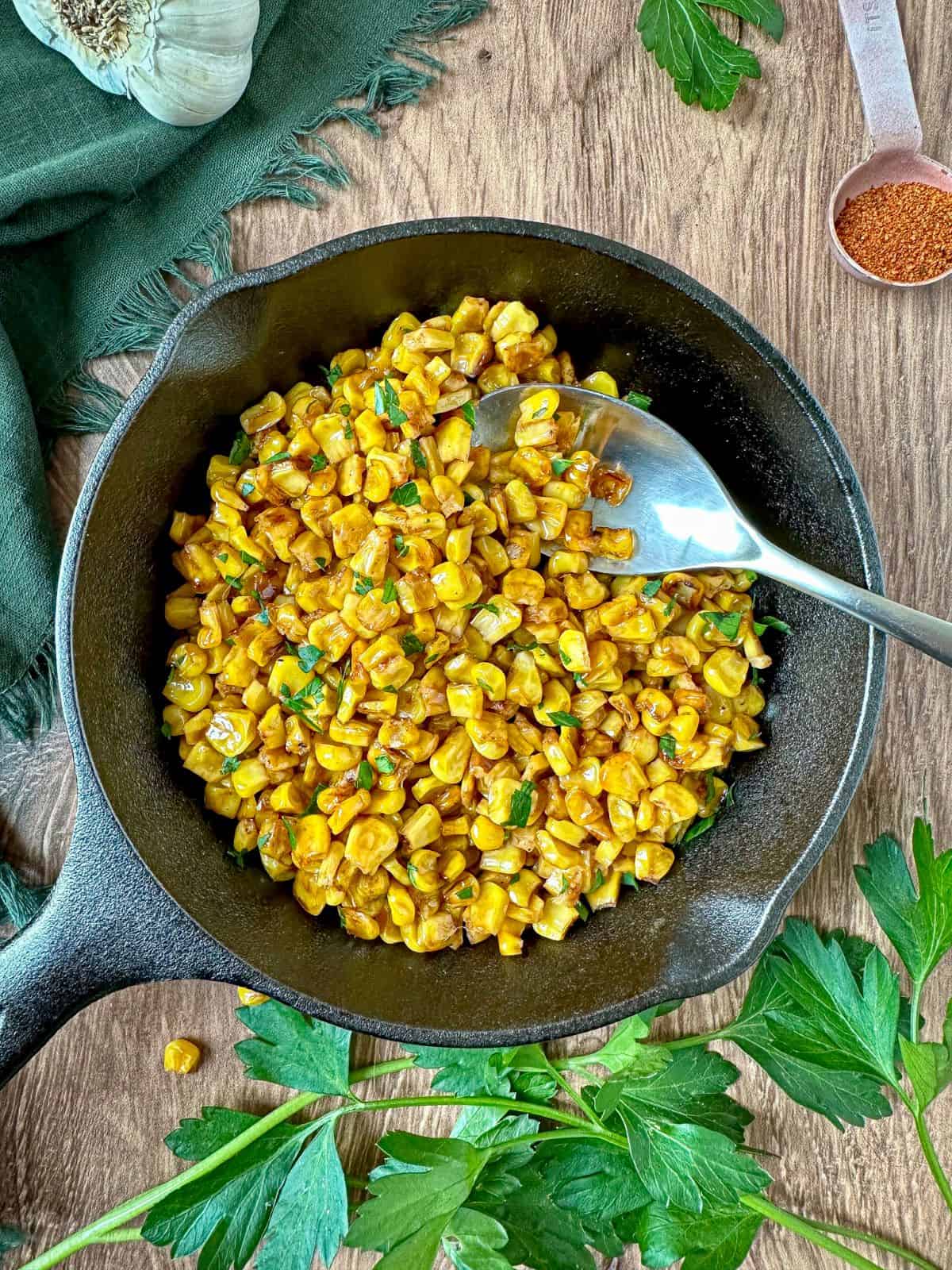 Charred corn in a cast iron skillet with a silver spoon.