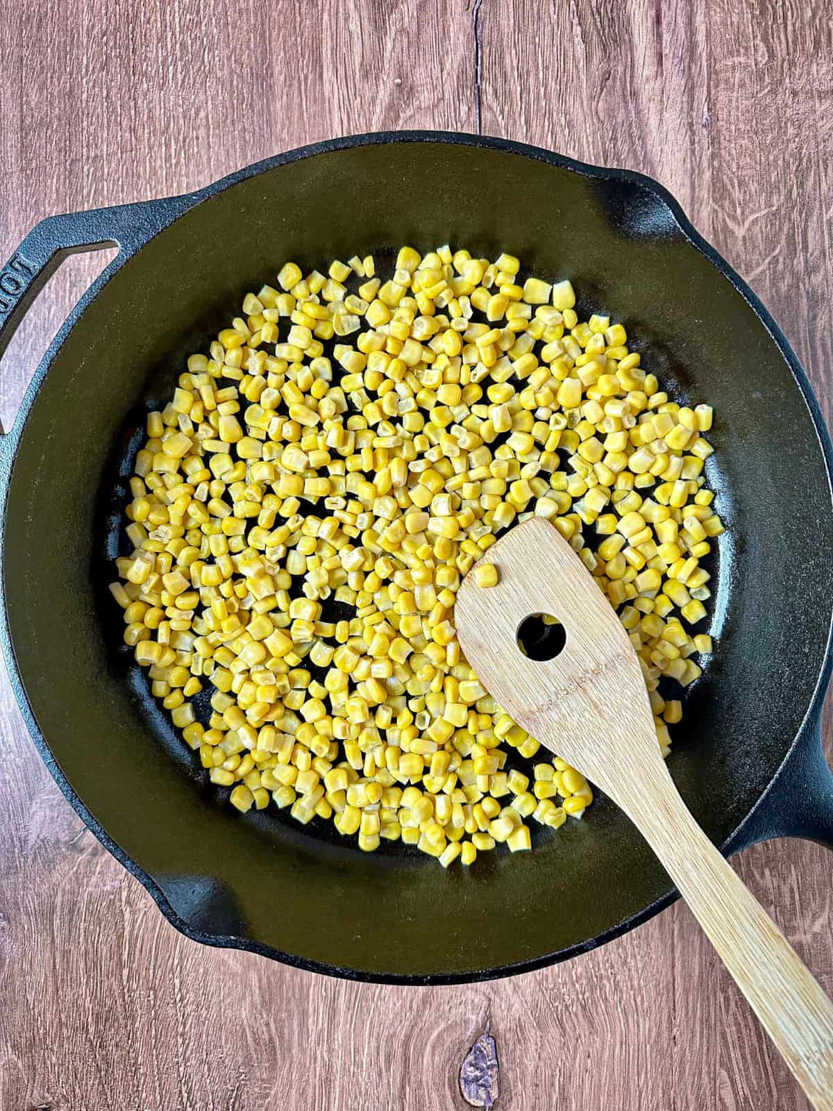 Corn in cast iron skillet with a wooden spoon.