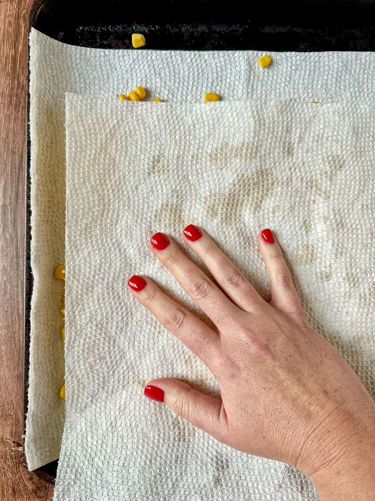 Hand patting dry corn kernels with a paper towels.