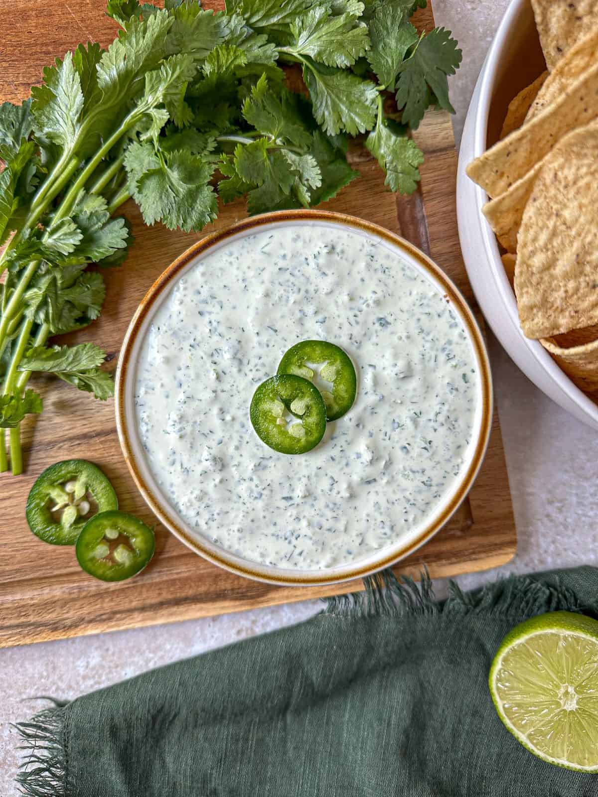 Creamy jalapeno sauce in a bowl surrounded by sliced jalapeno, cilantro, and tortilla chips.