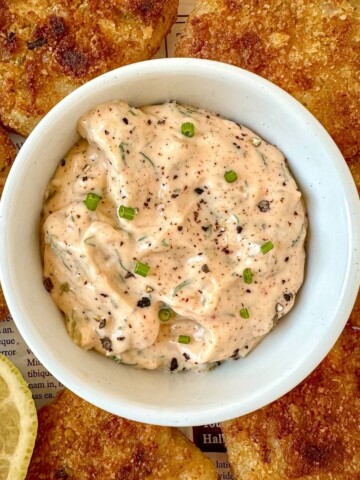 Homemade Cajun tartar sauce in a bowl surrounded by fried fish.