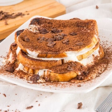 Three slices of tiramisu French toast with whipped cream stuffed in between the bread and a dusting of cocoa powder on top.