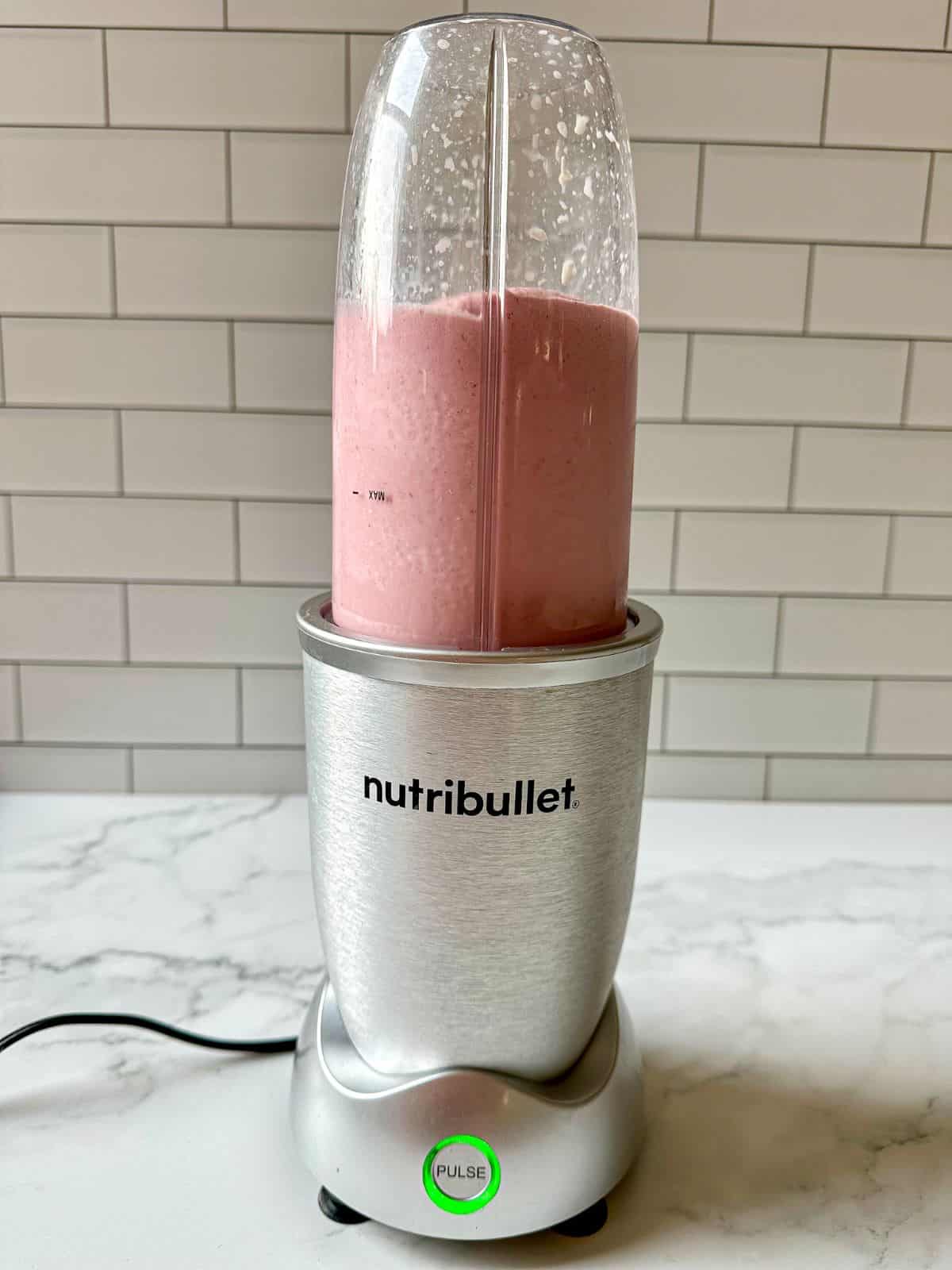A creamy pink smoothie getting blended in a blender.