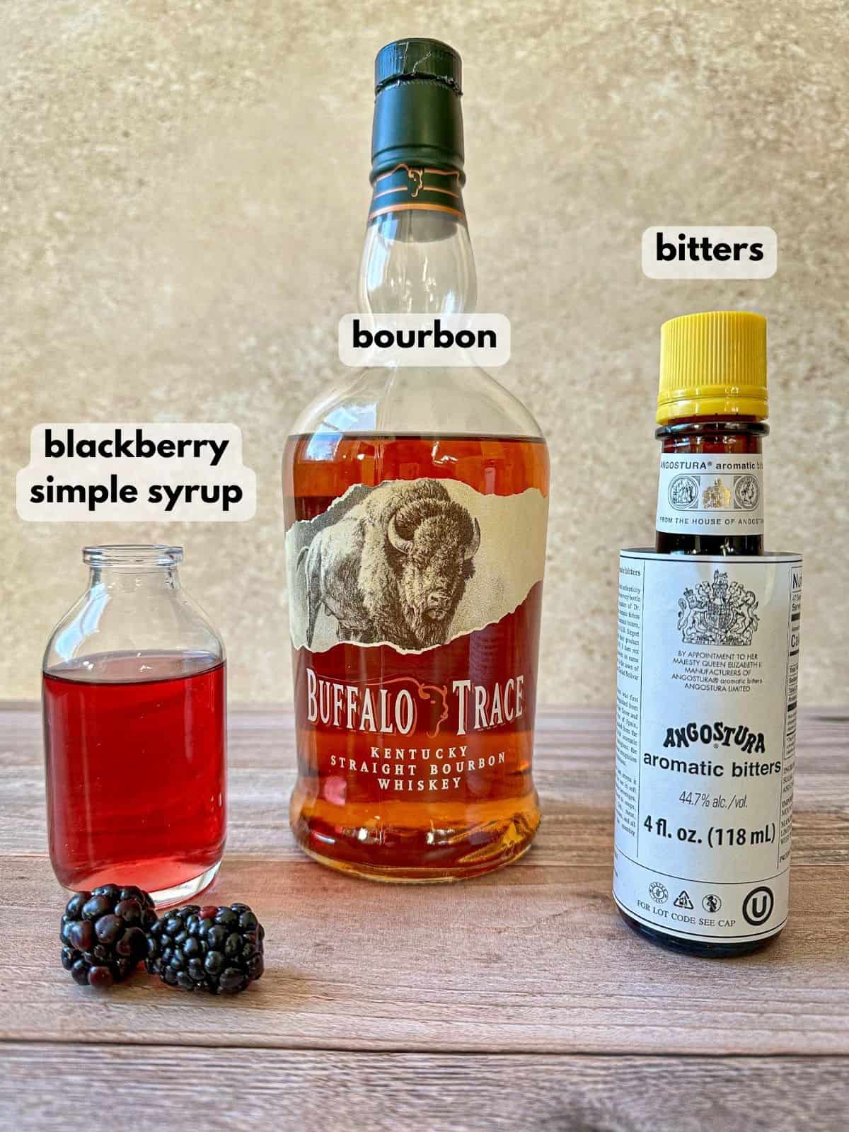 A bottle of bourbon, bitters, and a glass with blackberry syrup.