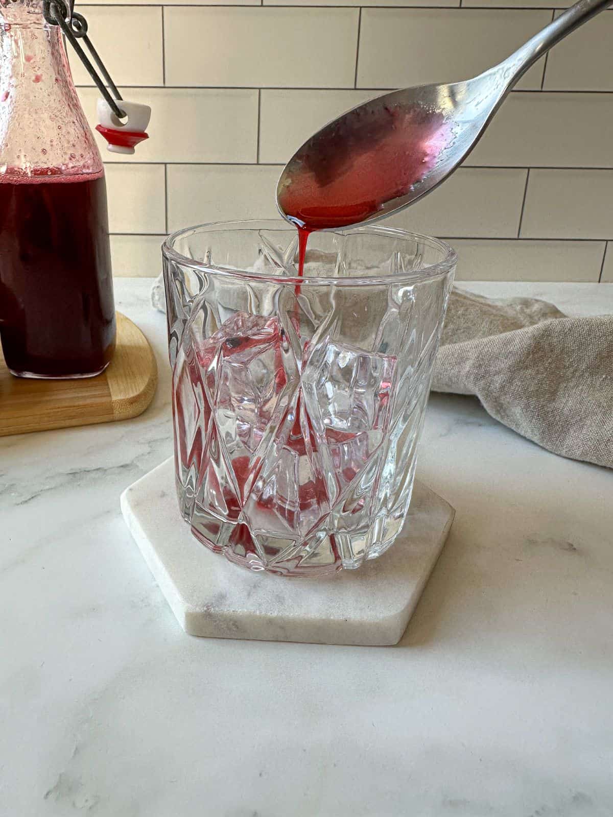 A spoon pouring blackberry syrup into a lowball cocktail glass with ice.