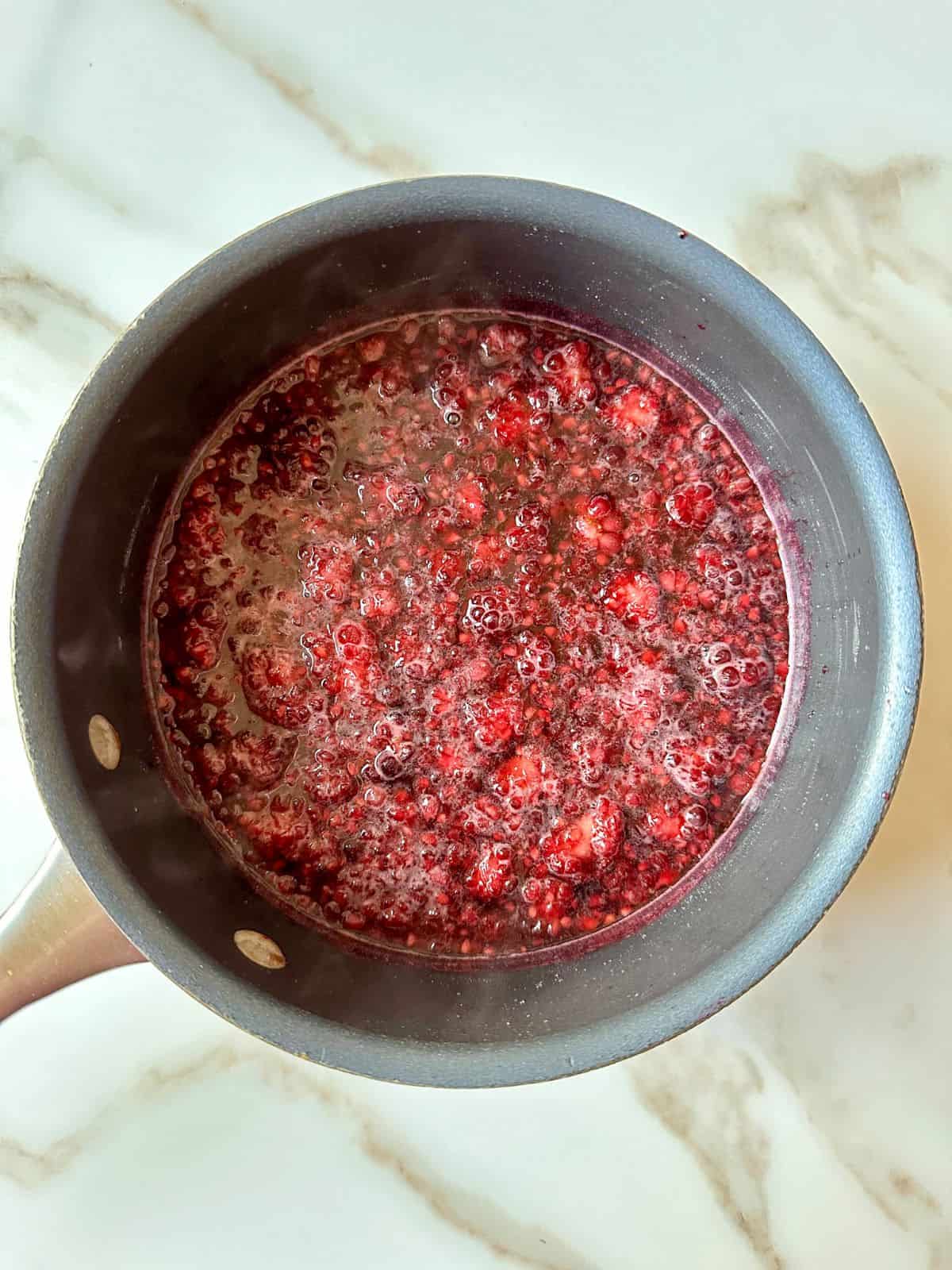 Purple colored liquid simmering in a saucepan with crushed blackberries.