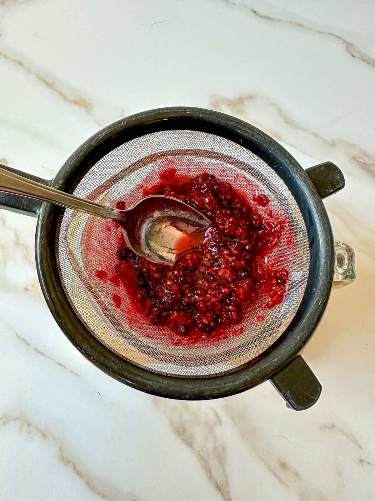 Blackberry seeds and solid pieces at the top of a strainer along with a spoon.