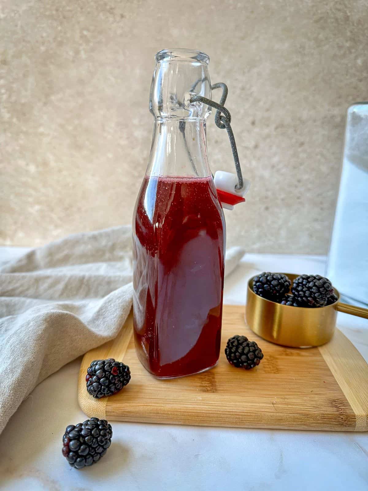 Glass jar filled with a purple blackberry simple syrup surrounded by fresh blackberries.