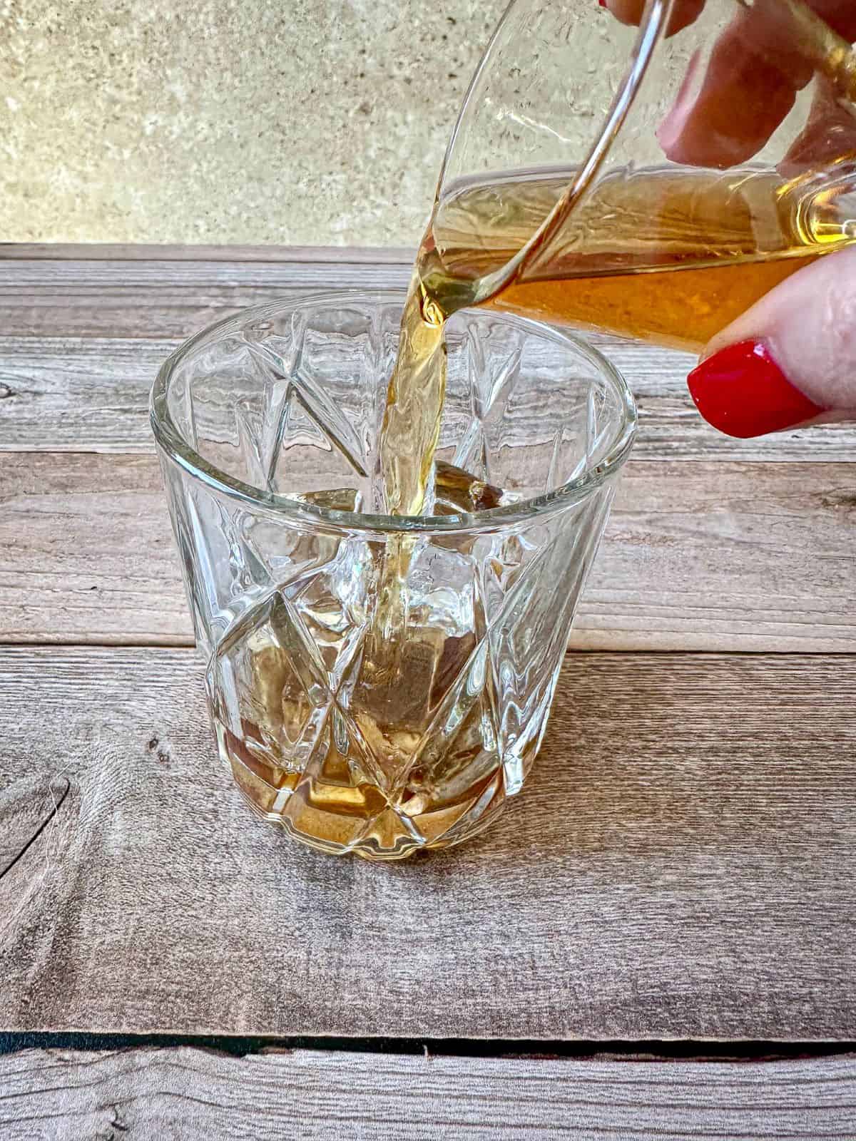 Hand pouring a shot of bourbon into a glass.