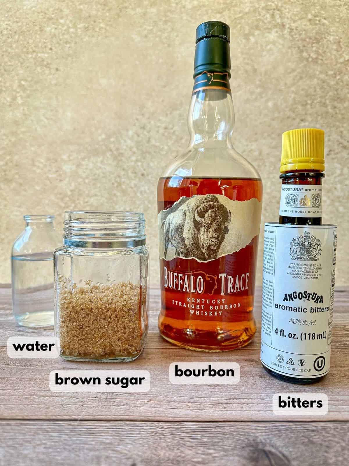 Bottle of bourbon, aromatic bitters, jar of brown sugar and glass of water.